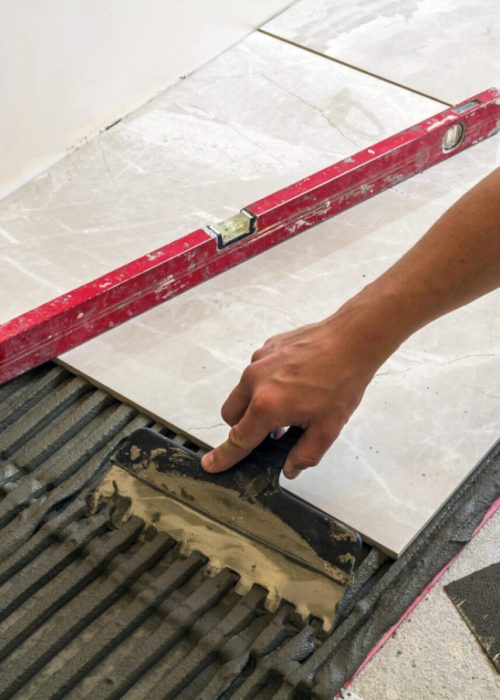 Ceramic tiles and tools for tiler. Worker hand installing floor tiles. Home improvement, renovation - ceramic tile floor adhesive, mortar, level