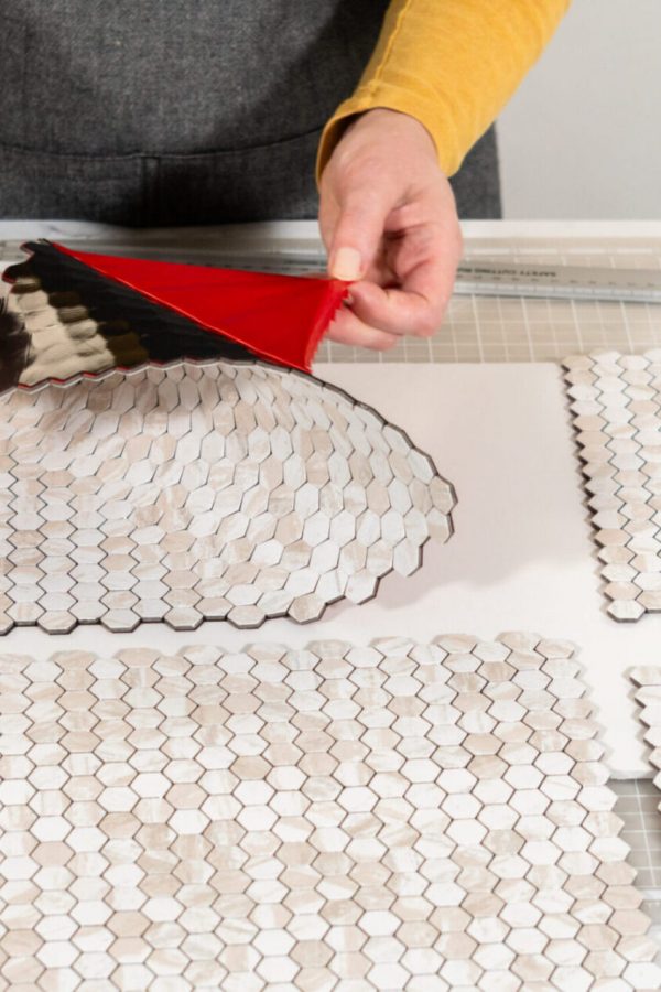 In the process of mounting peel and stick mosaic tiles onto a foam board, perfect for enhancing a food photography studio's aesthetic.