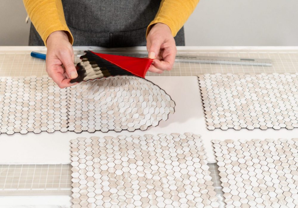 In the process of mounting peel and stick mosaic tiles onto a foam board, perfect for enhancing a food photography studio's aesthetic.