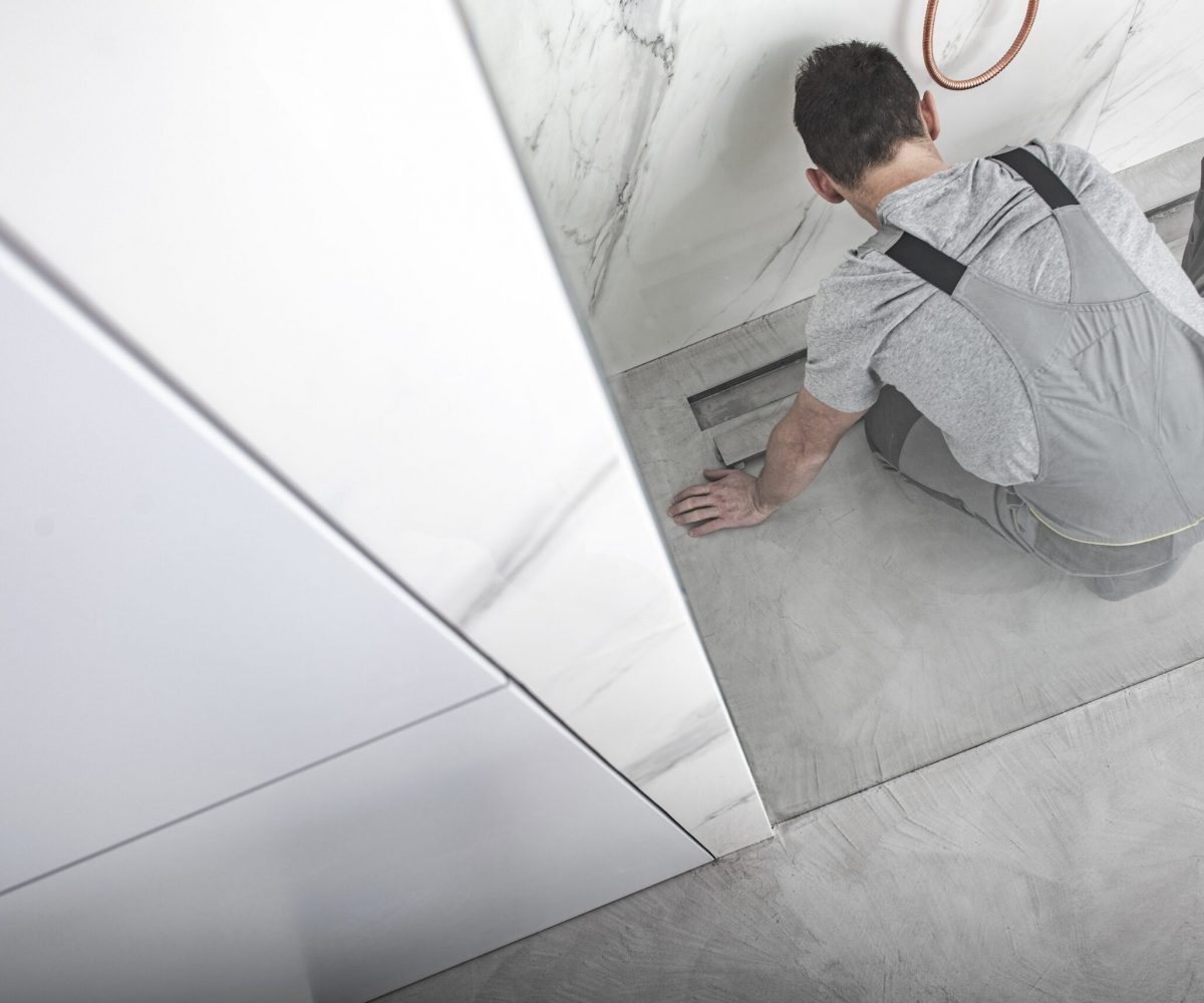 Caucasian Men Cleaning Linear Shower Drain. Top View Photo. Glassy Cabin. Modern and Stylish Bathroom Interior.