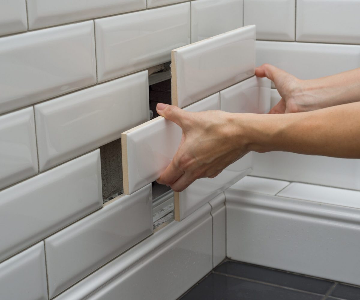 Woman opens, closes the hidden revision sanitary hatch on the wall of tile under the bathroom